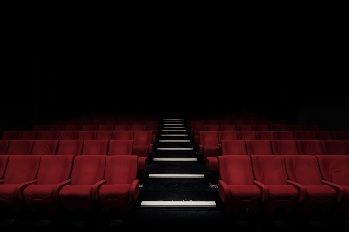 Empty movie theater with rows of red seats and a lit aisle evoking the shared cinema experience