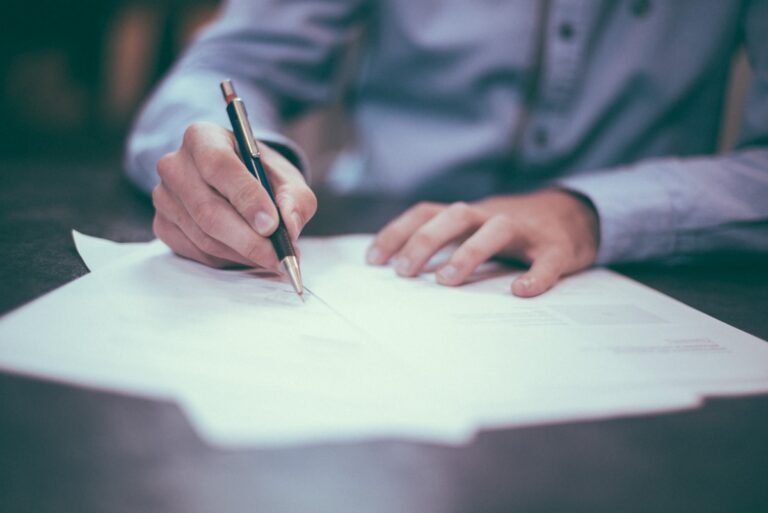 Person signing a document with a pen representing reviewing and choosing an insurance policy