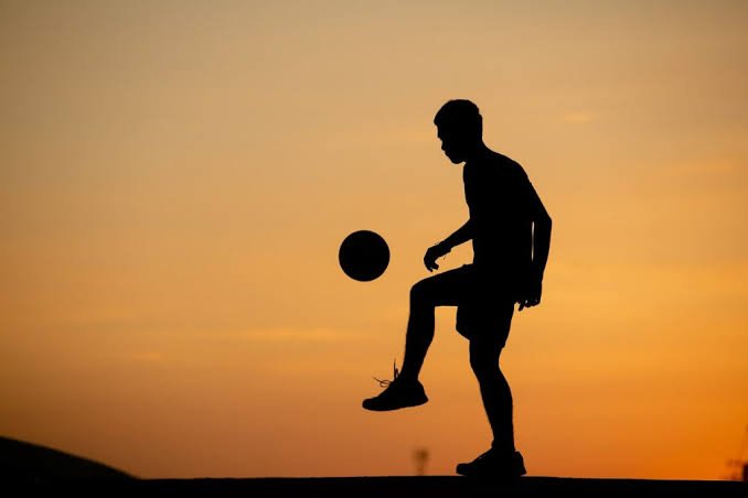 Silhouette of a footballer controlling a ball at sunset representing following a sports matchup